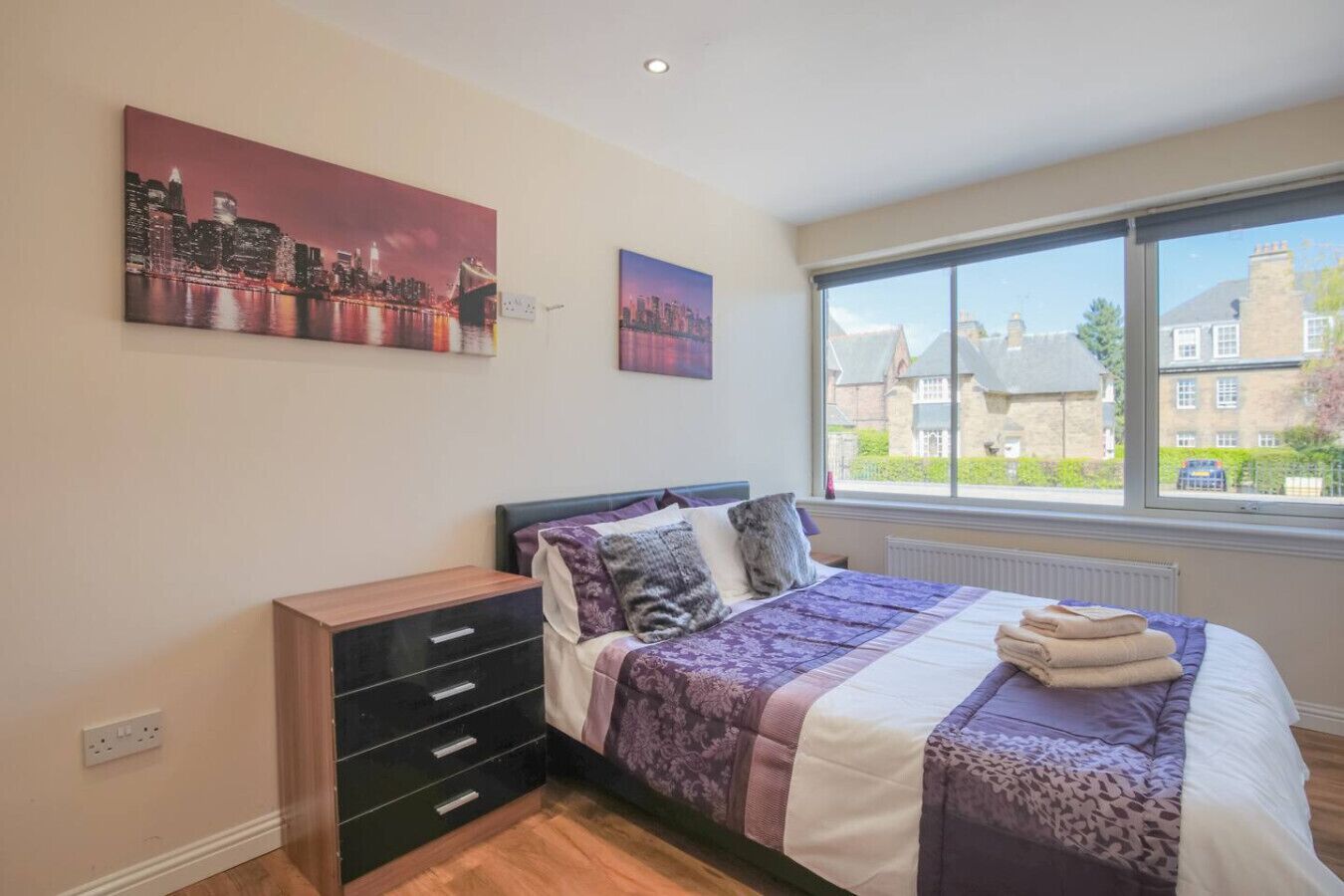Een slaapkamer met een bed, een kaptafel en twee schilderijen aan de muur.