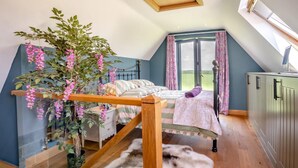 A bedroom with a bed, a wooden ladder, a hanging plant, a fur rug, and a view of the outdoors.