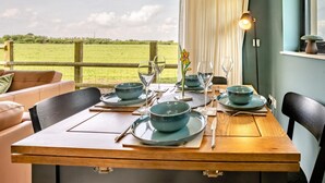 A dining table set with blue plates, glasses, and cutlery, with a view of a green field through a window.
