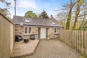 A stone cottage with a tiled patio, two wicker chairs, a small table, and a wooden fence. - 1 Bed in Lamorna (oc-k31904) (Lamorna)