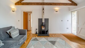 A cozy living room with a sofa, a patterned rug, a wood-burning stove, and a high ceiling with exposed beams. - 1 Bed in Lamorna (oc-k31904) (Lamorna)