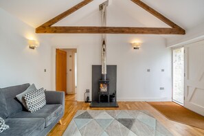 A cozy living room with a sofa, a patterned rug, a wood-burning stove, and a high ceiling with exposed beams. - 1 Bed in Lamorna (oc-k31904) (Lamorna)