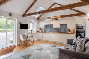 A modern kitchen with white cabinets, a dining area with a table and chairs, and a living area with a sofa. - 1 Bed in Lamorna (oc-k31904) (Lamorna)