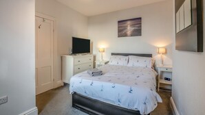 A bedroom with a bed, a television on a dresser, two bedside lamps, a painting on the wall, and a door. - 2 Bed in Scarborough (oc-s027) (Scarborough)