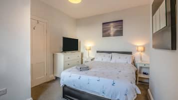 A bedroom with a bed, a television on a dresser, two bedside lamps, a painting on the wall, and a door.