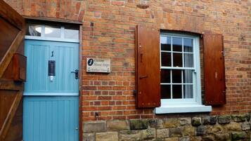 A brick building with a blue door and a window with wooden shutters. A sign on the wall reads "Custom House Steps, Harbour View."