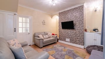 A living room with a grey sofa, a stone wall, a flat-screen TV, and a cabinet with a radio.