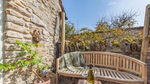 A stone building with a wooden bench and a table with a bottle and glasses.