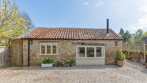 A stone house with a tiled roof, a wooden gate, and flower beds.
