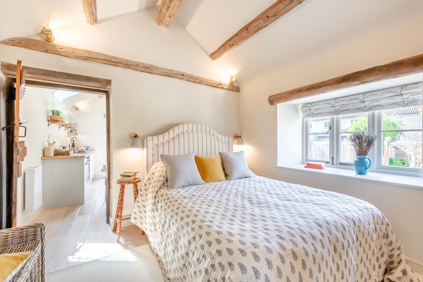 A bedroom with a bed, bedside table, lamp, and a window with a view.