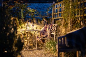 An outdoor seating area with a table and chairs, surrounded by a stone wall and vegetation.