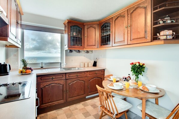 A kitchen with wooden cabinets, a dining table with chairs, a window with a view of the ocean, and breakfast items on the table. - 2 Bed in Scarborough (oc-s037) (Osgodby)