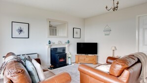 Ein Wohnzimmer mit Ledersofas, einem Kamin, einem Fernseher und gerahmten Bildern an der Wand.