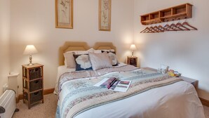 Un lit bien fait, recouvert d’une couvre-lit à motifs floraux, avec deux lampes de chevet et un porte-manteau en bois placé au-dessus.