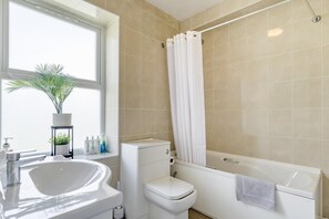 Ein Badezimmer mit Toilette, Waschbecken, Badewanne und einem Fenster mit Pflanze.