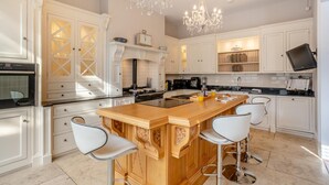 A modern kitchen with white cabinetry, a wooden island with bar stools, a built-in oven, and a chandelier. - 4 Bed in Beamish (oc-o32025) (Beamish)
