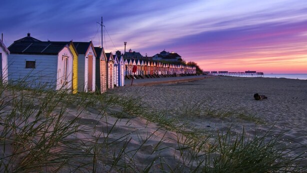 Une plage bordée d’une rangée de cabanes de plage aux couleurs vives et d’une jetée qui s’avance dans l’eau.