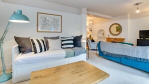 Un salon moderne avec un canapé blanc, un fauteuil bleu et une table basse en bois. On y trouve une lampe sur pied et un tableau encadré accroché au mur.