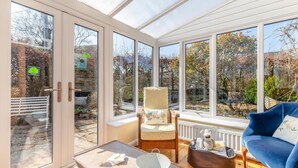 A conservatory with a chair, a blue sofa, and a table with a bucket. - 4 Bed in Onecote (oc-b31731) (Onecote)