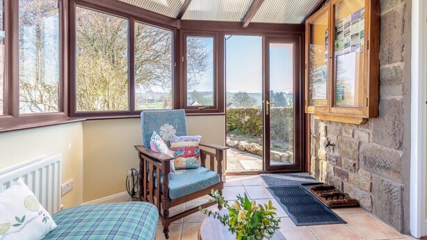 A sunroom with large windows, a wooden chair, a bed, and a stone wall. - 4 Bed in Onecote (oc-b31731) (Onecote)