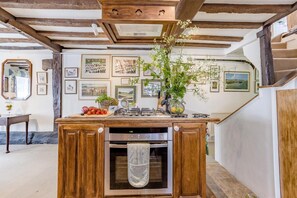 Une cuisine avec des meubles de rangement en bois, un four encastré et un îlot central doté d’un évier et d’une plaque de cuisson.