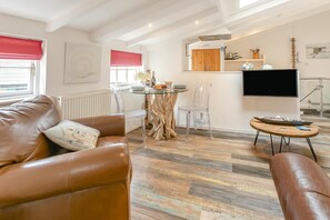 A modern living room with leather sofas, a glass dining table, and a flat-screen TV mounted on the wall. - 1 Bed in St. Ives (oc-drift4) (St Ives)