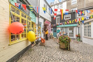 A cobblestone street with colorful flags, a shop with yellow windows, and a flower cart. - 1 Bed in St. Ives (oc-drift4) (St Ives)