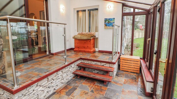 Une vaste terrasse avec un sol en pierre, un banc en bois et une porte vitrée donnant sur un jardin.