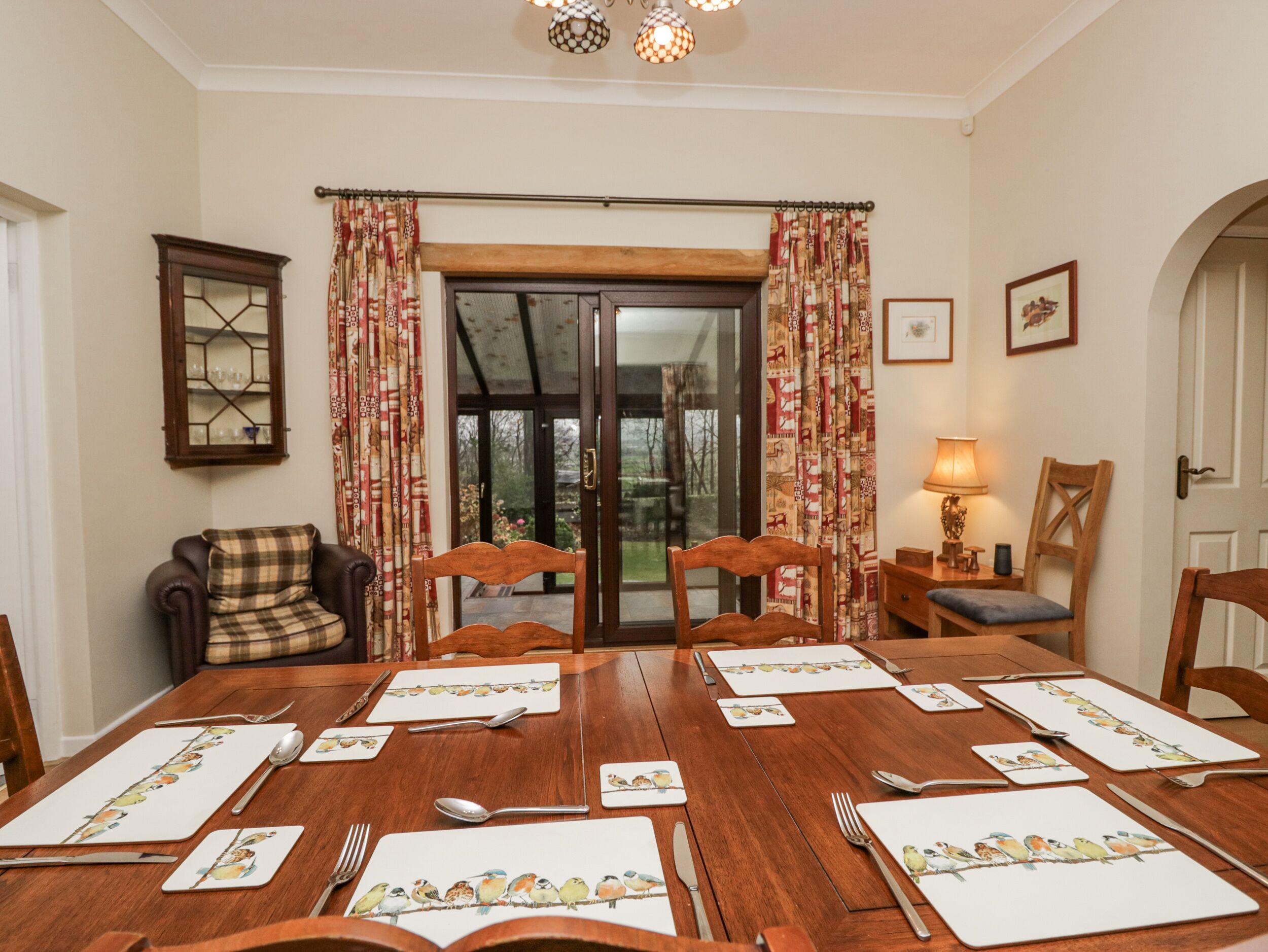 A dining room with a wooden table set for six, featuring bird-themed placemats.