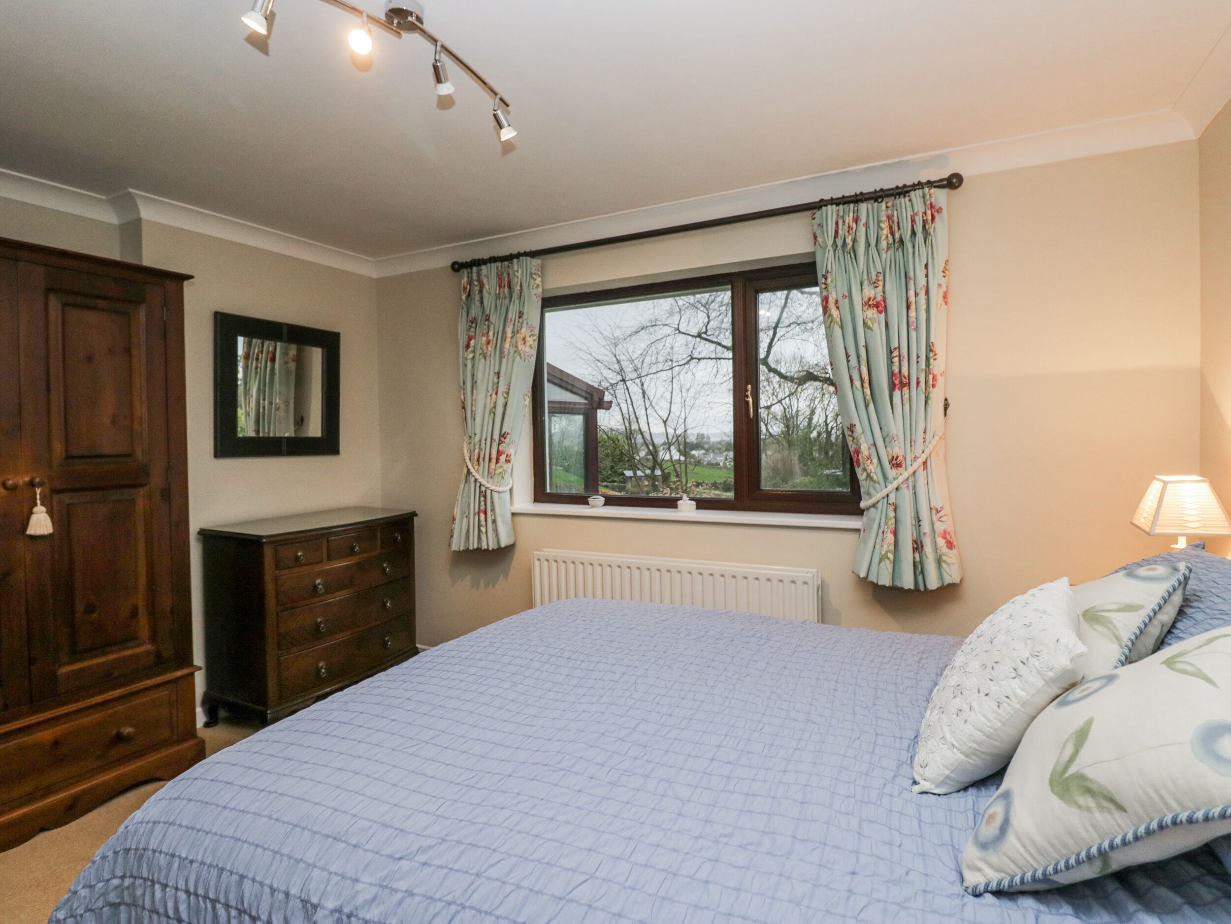 A bedroom with a large bed, wooden dresser, and a window with floral curtains.