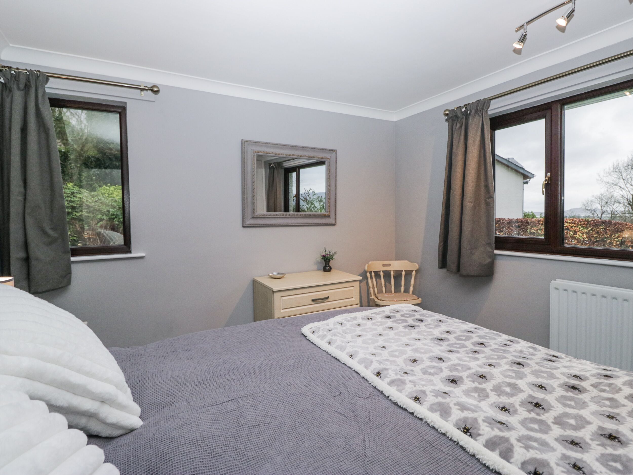A bedroom with a bed, dresser, chair, and a window with curtains.