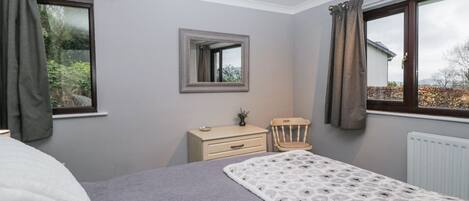 A bedroom with a bed, dresser, chair, and a window with curtains.