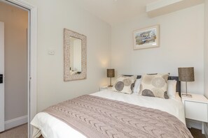 Ein Schlafzimmer mit einem Bett, einem Nachttisch, einer Lampe, einem Spiegel und einem gerahmten Bild an der Wand.