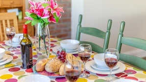 Ett dukat bord för en måltid, med en vinflaska, bröd, en vas med blommor och glas med rött vin.