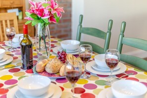 Ein Esstisch ist gedeckt mit einer Weinflasche, Brot, einer Blumenvase und Weingläsern.