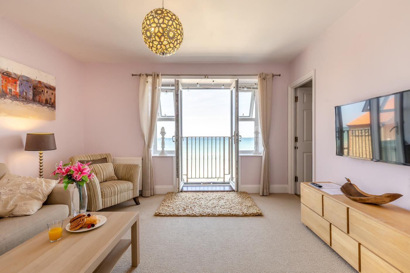 A living room with a sofa, a coffee table with breakfast, a TV, and a balcony with a view.