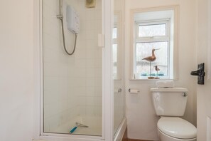 Une salle de bain avec une douche à parois de verre, des toilettes et une fenêtre décorée avec un motif d’oiseau.
