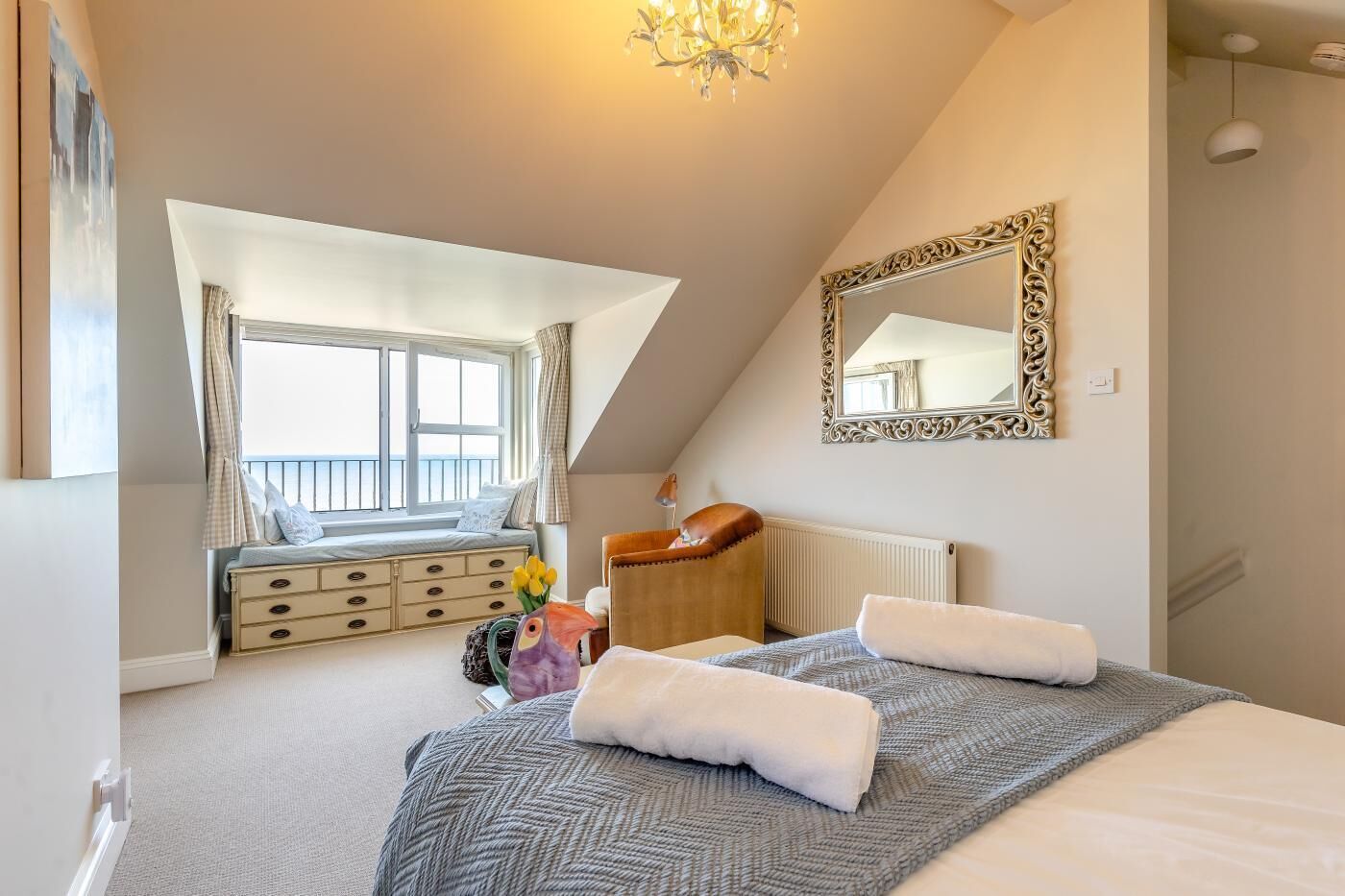 A bedroom with a large bed, a window with a view, a dresser, a chair, and a mirror on the wall.