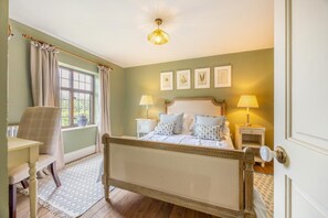 Une chambre à coucher comprenant un lit, des tables de chevet, une chaise, une fenêtre avec des rideaux et des reproductions encadrées de motifs botaniques au mur.
