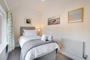 A hotel room with a bed, a nightstand, a lamp, a painting, and a window with curtains. - 4 Bed in Cromer (oc-2069) (Cromer)