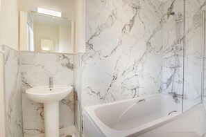 A bathroom with a marble wall, a sink, and a bathtub.