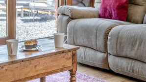 A cozy living room with a wooden coffee table, a beige sofa, and a window with a view of outdoor seating. - 3 Bed in Llangadog (oc-c32033) (Llangadog)