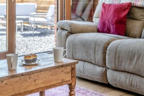 Un salon chaleureux avec une table basse en bois, un canapé beige et une fenêtre donnant sur un espace extérieur aménagé avec des sièges.
