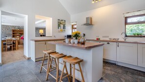 A modern kitchen with a central island, bar stools, a stone accent wall, and a large window. - 3 Bed in Llangadog (oc-c32033) (Llangadog)
