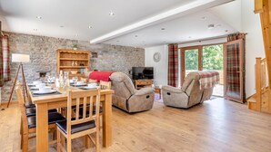 A spacious living area with a stone wall, wooden furniture, and a large window providing a view of the outdoors. - 3 Bed in Llangadog (oc-c32033) (Llangadog)
