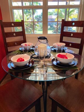 A round glass table with four chairs, a pitcher, and bowls with red decorations.