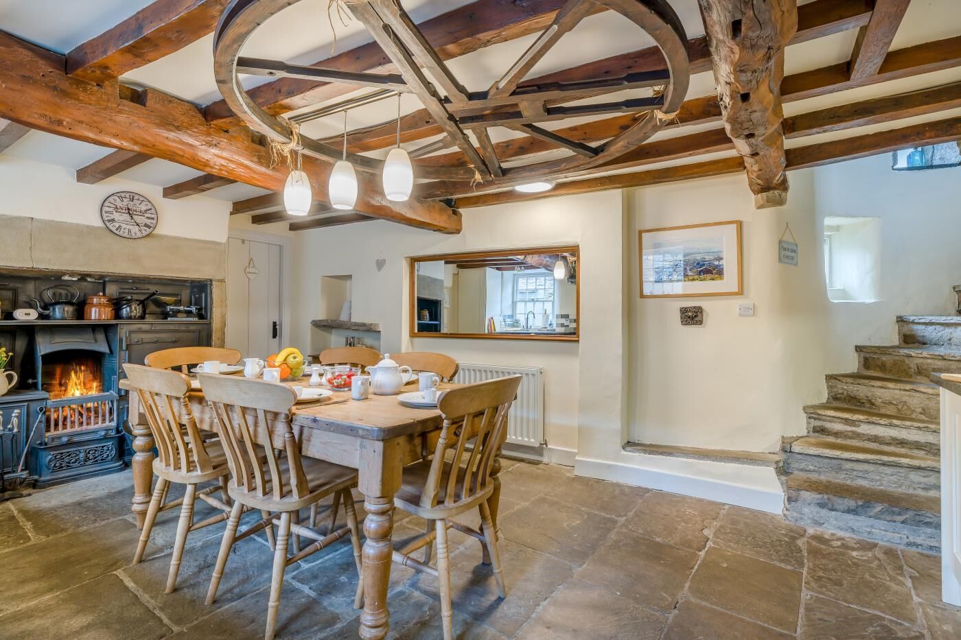Une cuisine rustique avec un sol en pierre, des chaises en bois, une table à manger, une cheminée et un miroir au-dessus de la table.