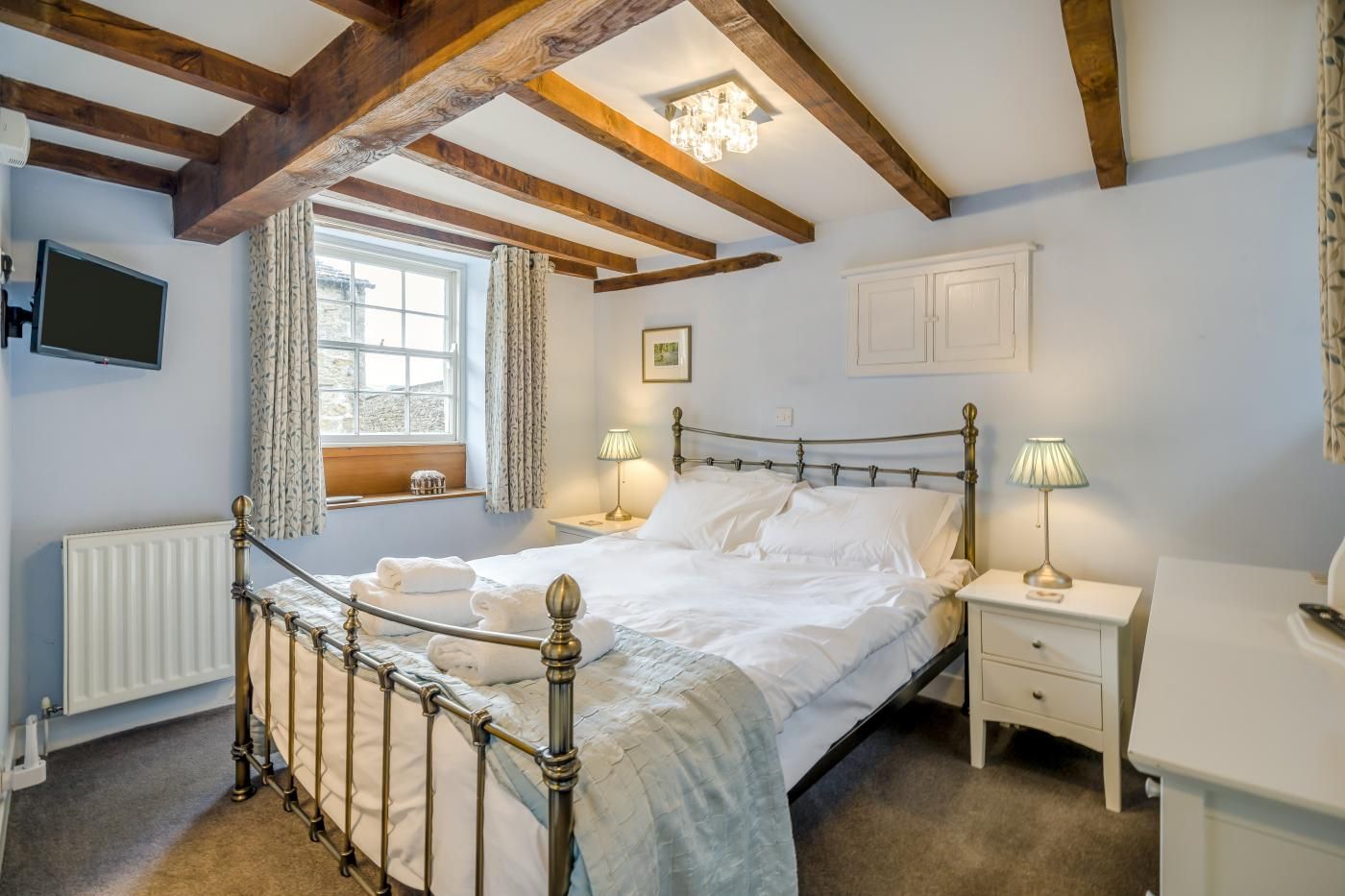 A bedroom with a four-poster bed, bedside lamps, a radiator, a window with curtains, and a white wardrobe.