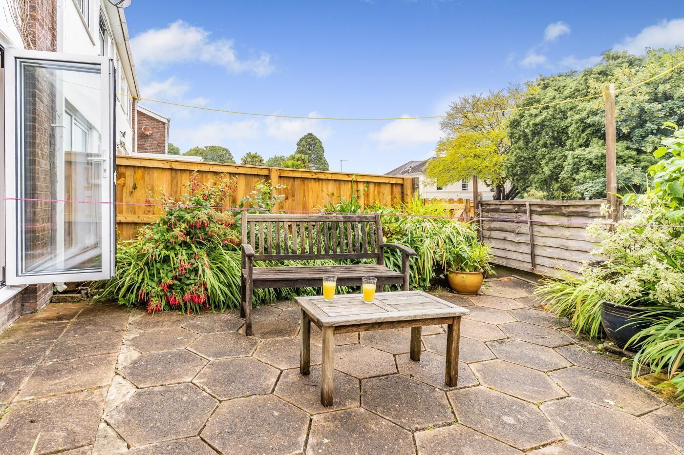 A patio with a wooden bench and table, surrounded by potted plants and a wooden fence.