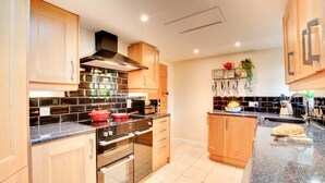 Une cuisine moderne avec des meubles en bois, une hotte en acier inoxydable, un plan de travail noir et un pare-feu en carreaux.